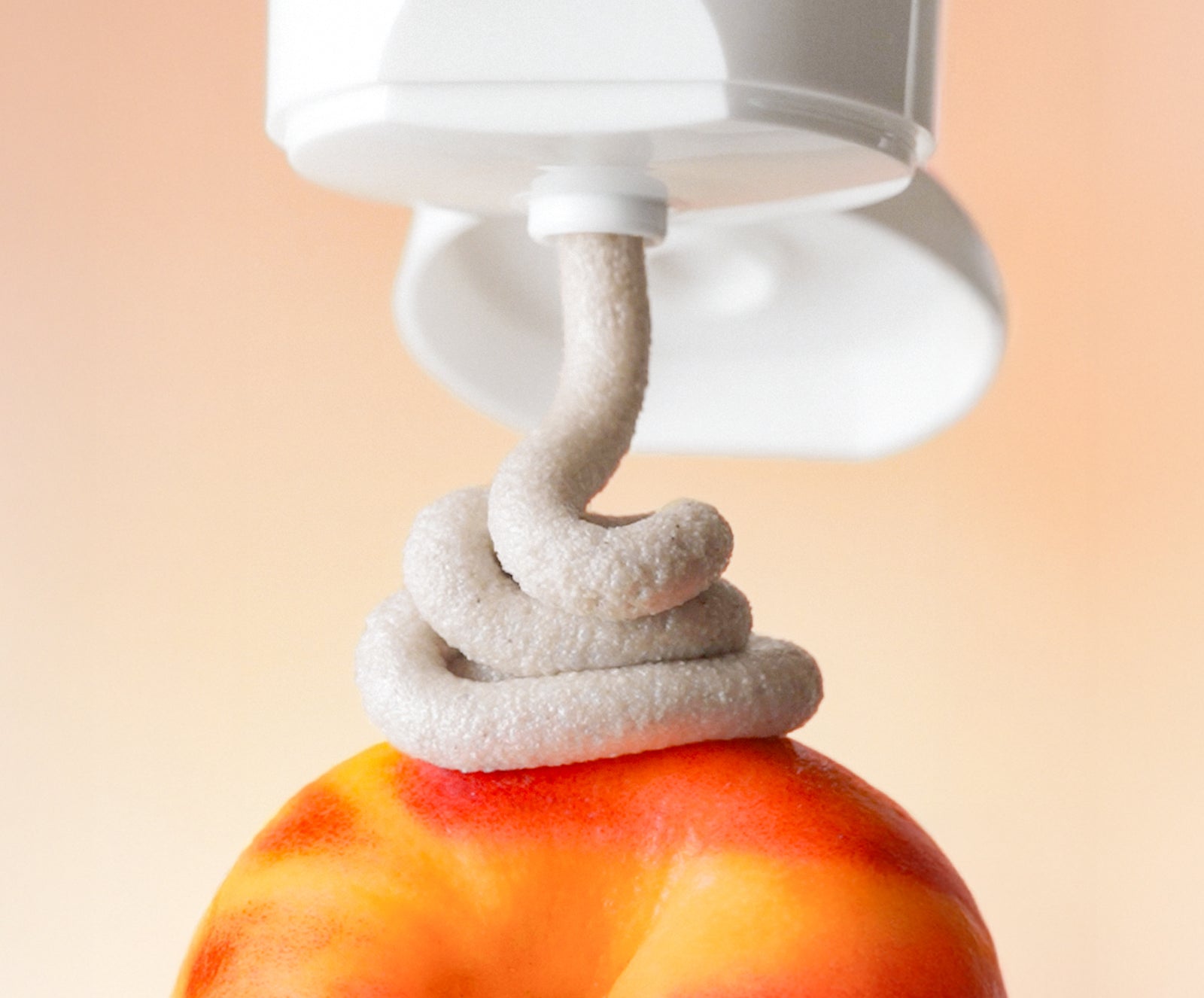 White KP Scrub being squeezed on a peach with a light beige background to show paste texture