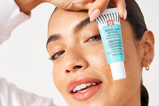 Woman holding Brighten and Glow Eye Cream in front of her face